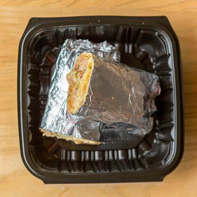 Halved burrito wrapped in foil in a takeout container.
