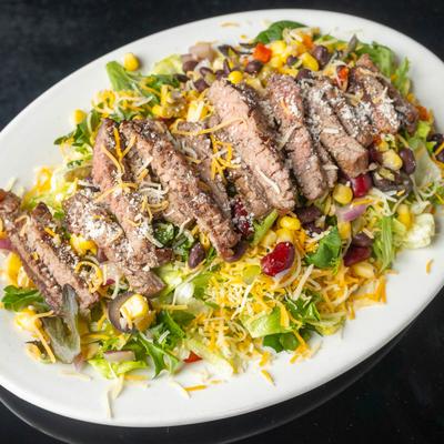 Grilled steak over a lettuce salad with corn, beans, and shredded cheese.