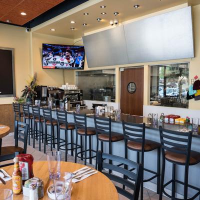 Interior, bar featuring a long counter with high chairs, and a TV showing a sports event.