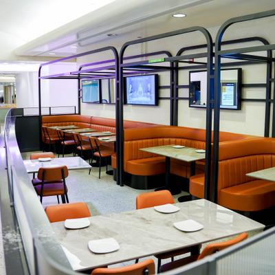 Orange upholstered booths and tables in an indoor dining area with televisions on the wall.