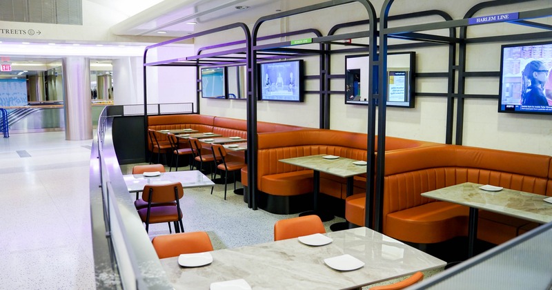 Orange upholstered booths and tables in an indoor dining area with televisions on the wall