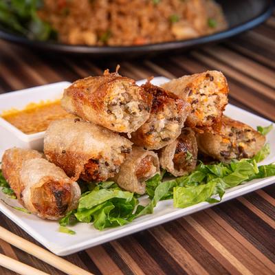 Crispy fried spring rolls stacked on greens with dipping sauce.