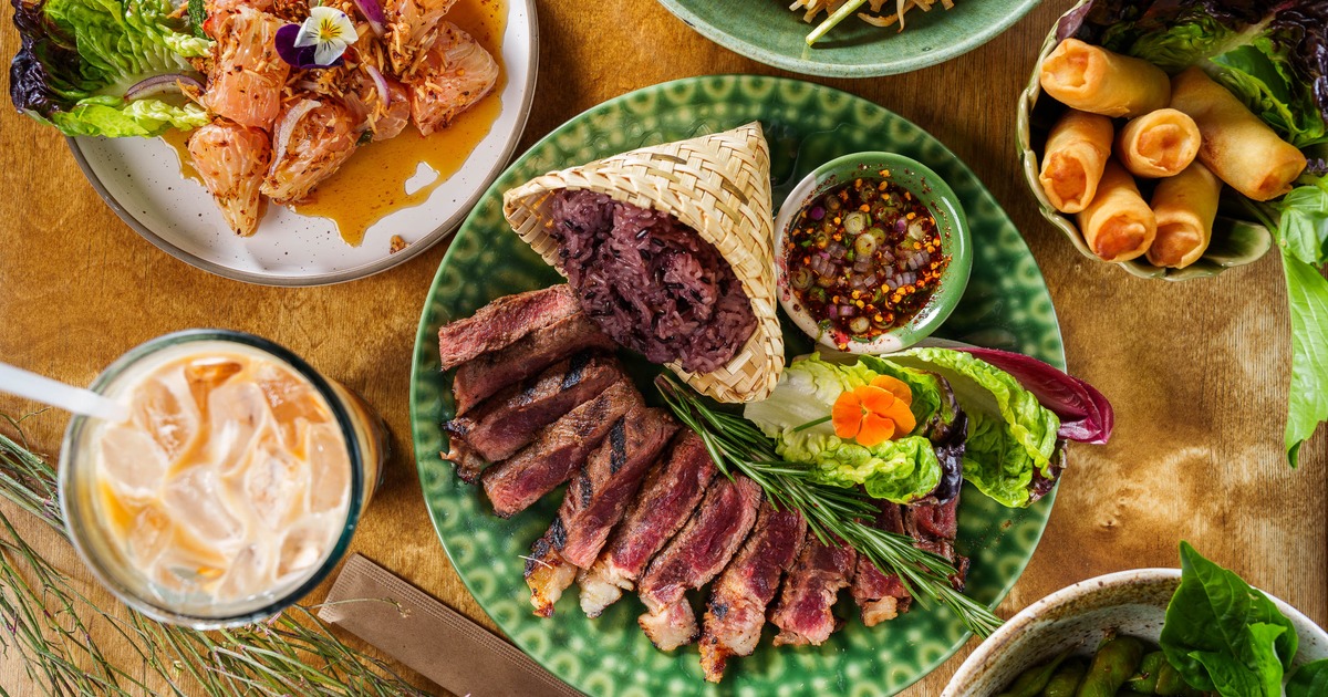 Crying Tiger steak with sides served alongside other dishes and a drink