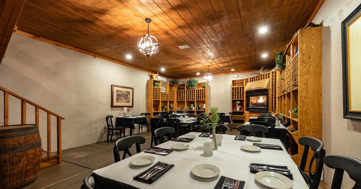 A small room with set tables, chairs and wooden wine racks alongside the walls