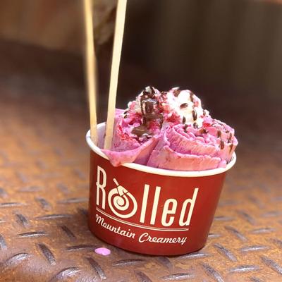 Bright pink ice cream with sprinkles in a red cup.