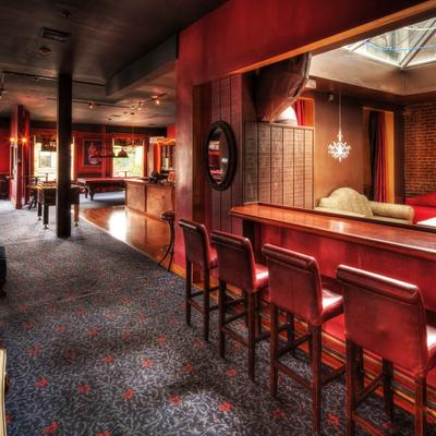 Elegant bar interior with red walls and carpet, featuring wooden stools along a polished bar
