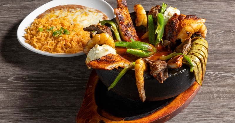 Molcajete dish with grilled steak, chicken, shrimp, cactus, cheese and sides of rice and beans