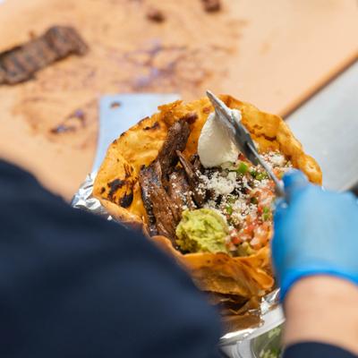 Person preparing a steak taco salad served in a crispy flour tortilla bowl.