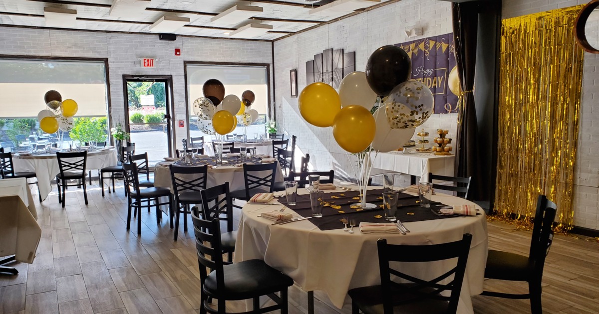 Party room features tables with black and gold balloons, festive table settings