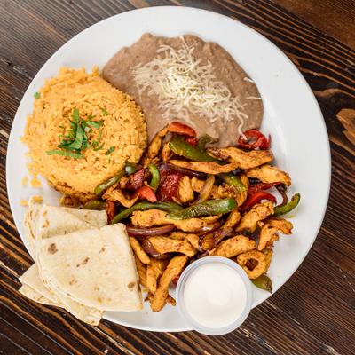 Chicken fajitas served with rice, refried beans, sour cream, and tortillas.