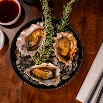 Grilled oysters with rosemary garnish served in a bowl with hot stones.