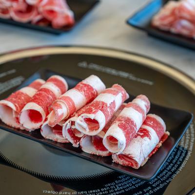 Thin-sliced beef belly rolls served on a black plate.