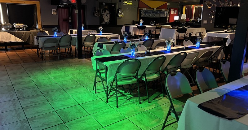 Room set for a party, with long tables covered in white and black cloths, blue glowing centerpieces
