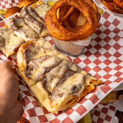 A hand holding a tray with the Sliced Steak Sandwich.