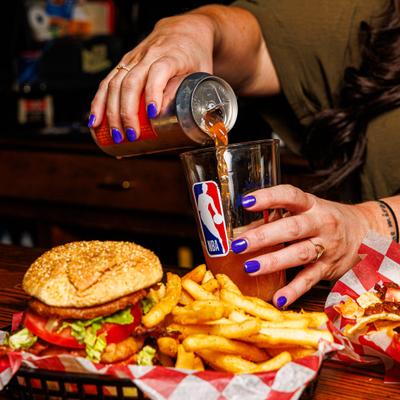 A burger, fries, and a beverage being poured into an NBA pint glass.