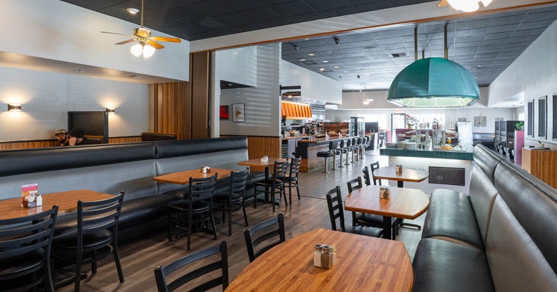 A spacious restaurant interior with wooden tables and black chairs