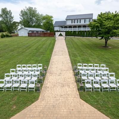 Lawn with a paved aisle in the middle and white chairs on both sides.