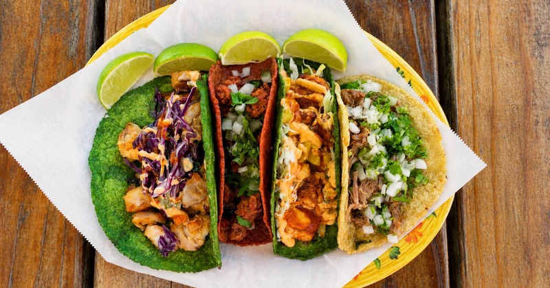 Plate of four assorted Mexican tacos garnished with lime wedges