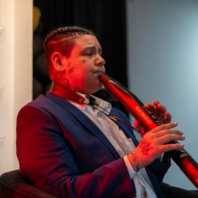 A musician in a blue blazer plays a red electronic wind instrument.