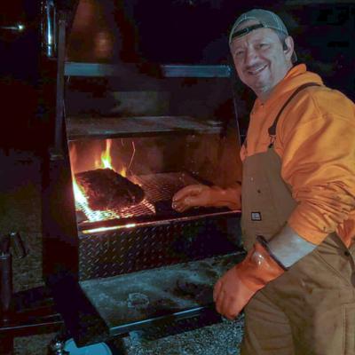 The chef tending to a grill with flames, grilling a piece of meat.