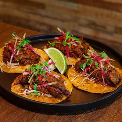 Barbacoa beef tacos topped with herbs, served with a lime wedge.