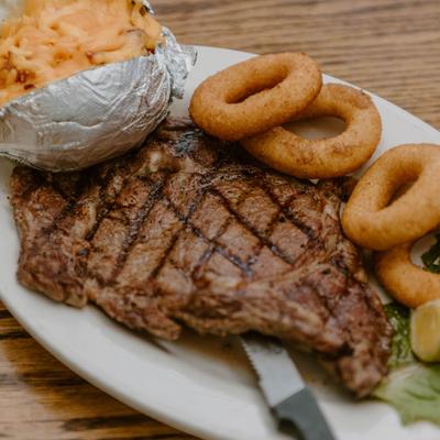 Grilled ribeye steak with baked potato and onion rings.