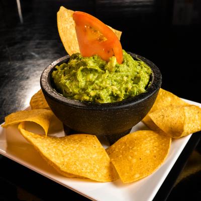 Guacamole garnished with a tomato slice and served with tortilla chips.