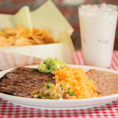 Grilled steak, served with guacamole, rice, and refried beans.