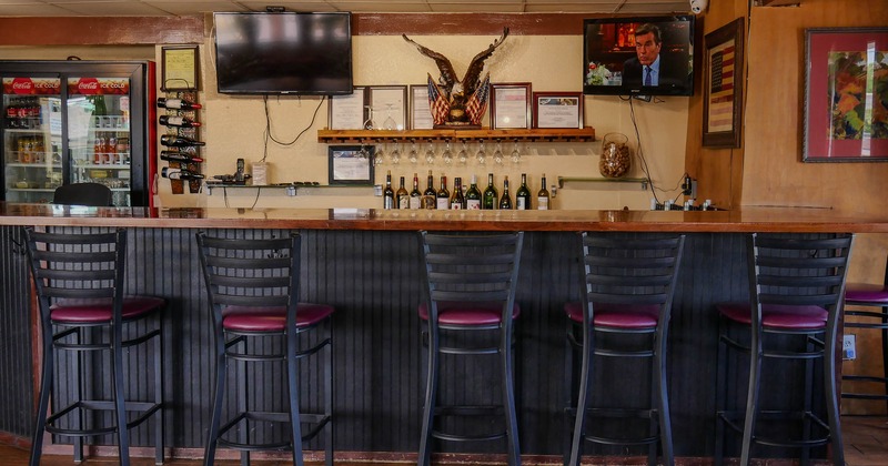 Interior, bar area, wooden top bar with stools, drink shelf in the back, TVs on the wall