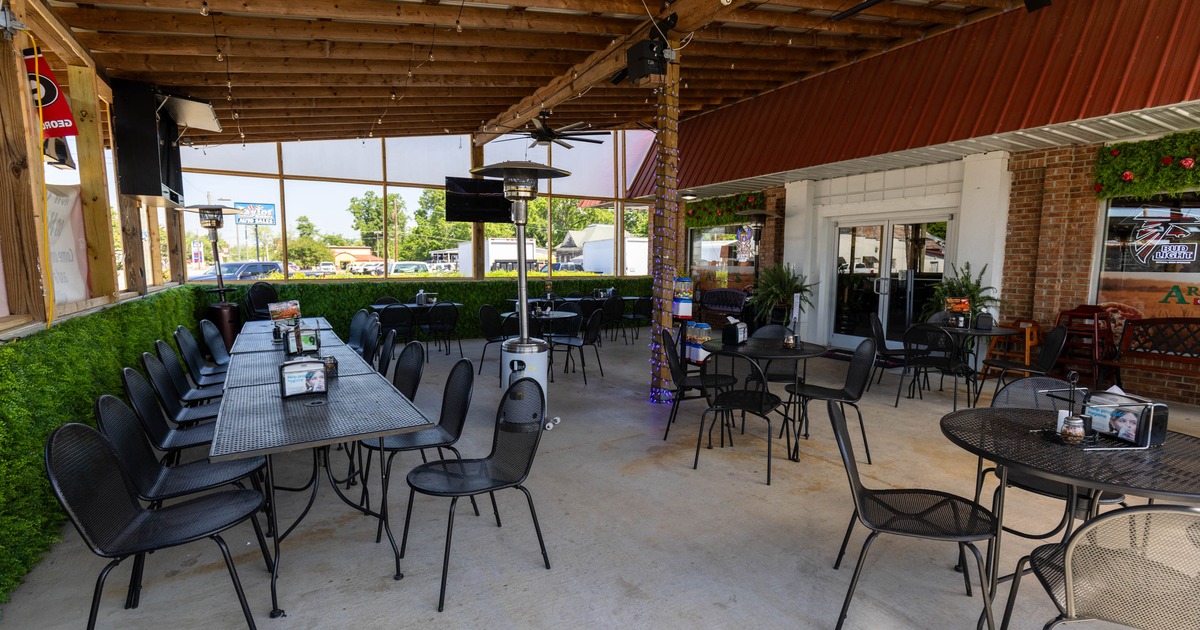 Outdoor seating area - black metal tables and chairs under a wooden pergola with string lights