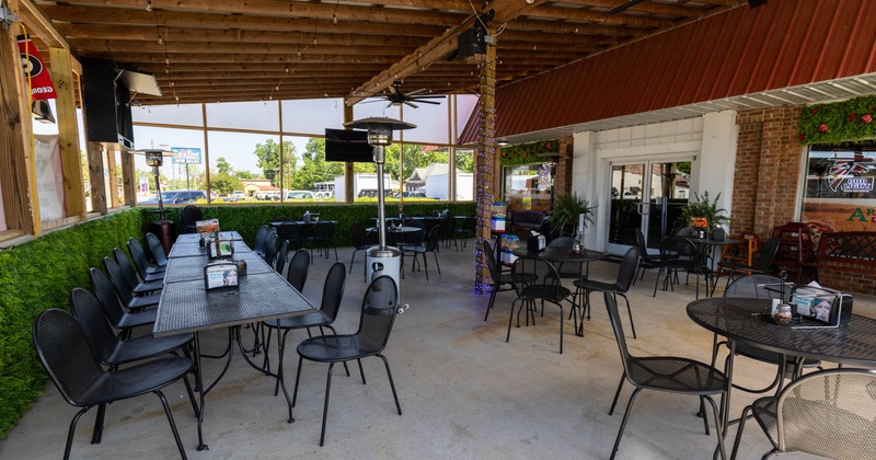 Outdoor seating area - black metal tables and chairs under a wooden pergola with string lights