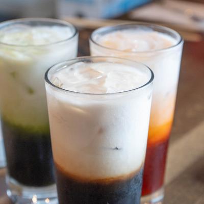 Three layered iced drinks served in clear glasses with dark bases.