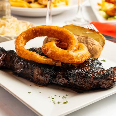 Grilled steak topped with onion rings, served with a baked potato
