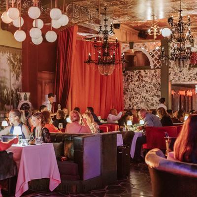 Main dining area at capacity with tables fully seated, chandeliers overhead and red curtains in the background.