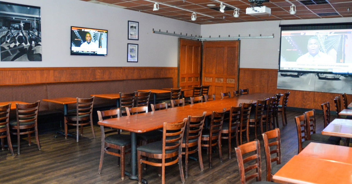 Dining area with tables and chairs, and one large table in the middle. Two TVs above on the walls