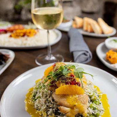 Pan Roasted Grouper plate with a glass of white wine and food behind it.
