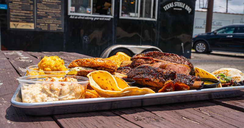 Barbecue platter with smoked meats, tacos, coleslaw, and macaroni on tray