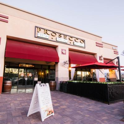 Prosecco restaurant exterior with signage, red awning, and patio seating.