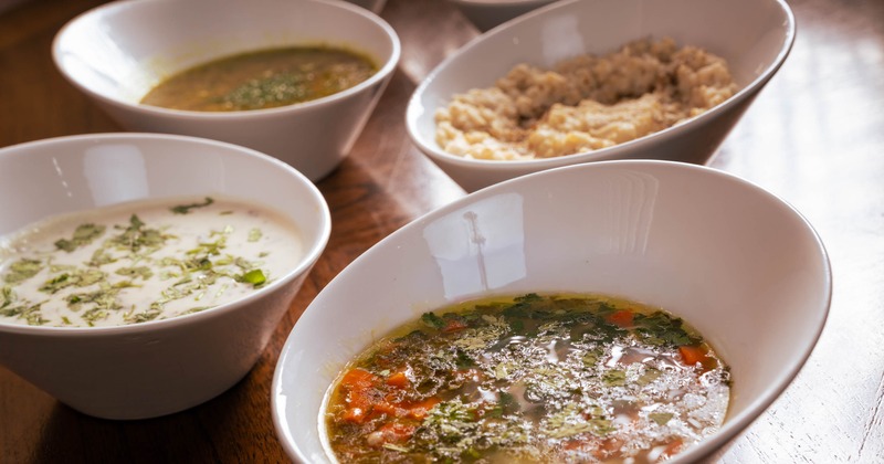 Four white bowls filled with different soups on a table