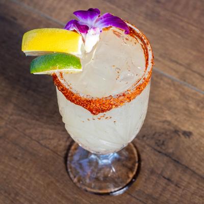Margarita served in a chili-rimmed glass with citrus and flower garnish.