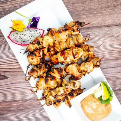 Chicken Satay Skewers served with a dopping sauce and piece of dragon fruit.