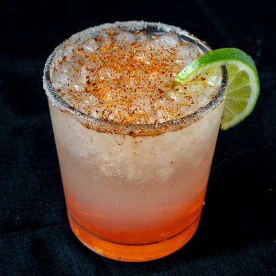 Paloma cocktail with crushed ice, chili salt, and lime garnish.