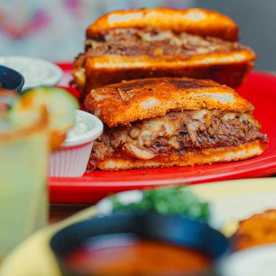 Torta sandwich on a red plate with a cocktail in the foreground.