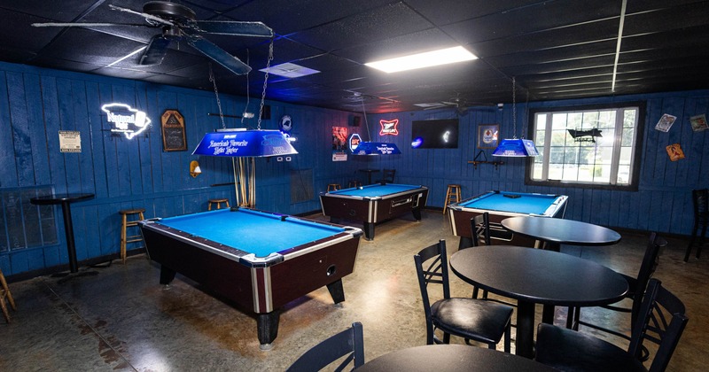 Billiards room with blue felt pool tables, neon lights, blue walls and round black tables and chairs