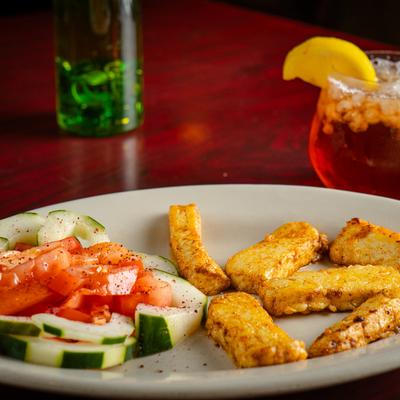 A plate with fried cheese and a cucumber-tomato salad on a red table with tea and a green vase.