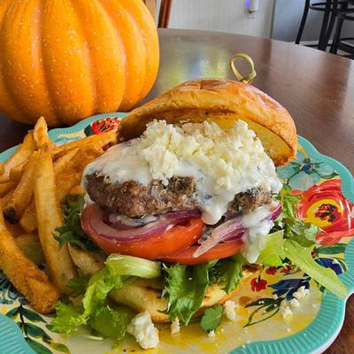 A colorful hamburger topped with cheese and sauce, served with fries, beside a pumpkin.