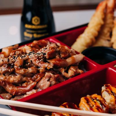 Bento box, with teriyaki chicken, shrimp tempura, sauce, and sushi rolls.