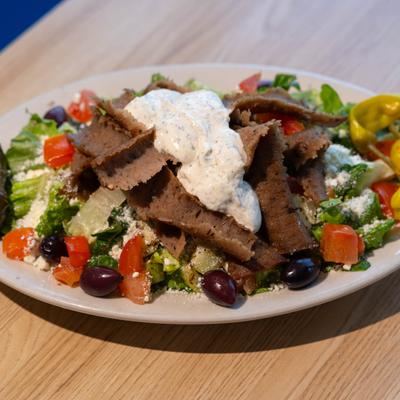 Gyro salad topped with sliced meat, tzatziki, olives, and vegetables.