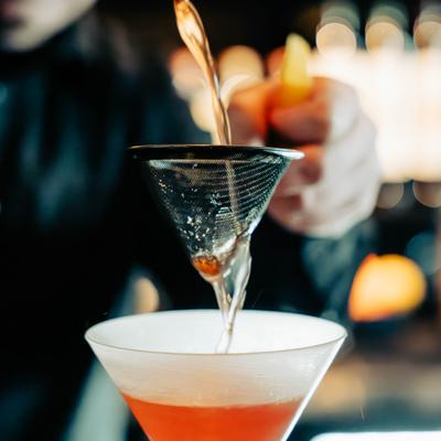 Bartender pouring a cocktail through a strainer - Paper Plane.