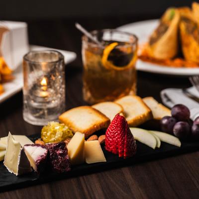 Cheese Plate with varios fruits, nuts and toasted bread, served alongside a cocktail.